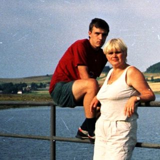 Couple posing by lake with scenic hillside.