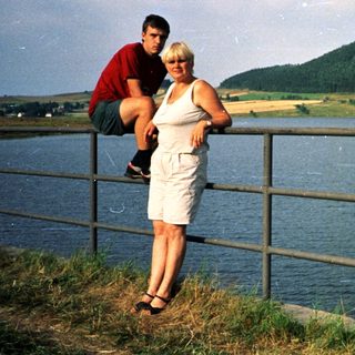 Couple posing by lake with scenic hillside.