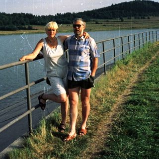 Couple posing by lake with scenic background.
