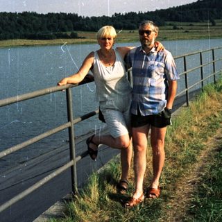 Couple posing by lake with scenic background.