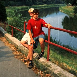 Boy in red shirt poses by wet path near river.