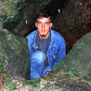 Person peeking from narrow cave entrance.
