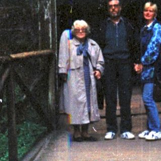 Three people standing on a wooden bridge leading into a dark cave entrance.