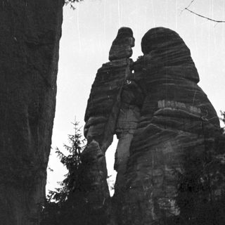 Two figures silhouetted on rock formations in rain.