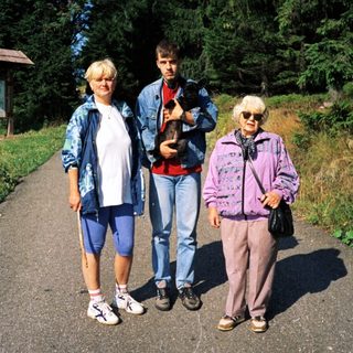 Three people hiking with a dog in a forested area.