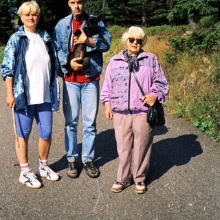 Three people hiking with a dog in a forested area.