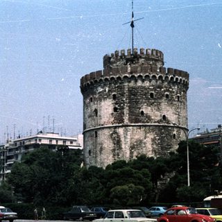 Historic tower in urban area with parked cars.