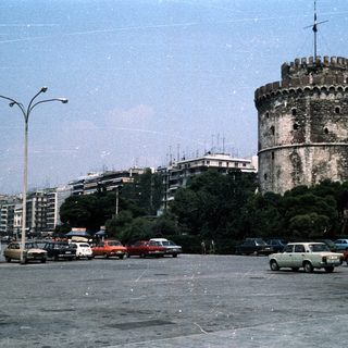 Historic tower in urban area with parked cars.