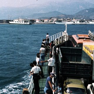 Ferry passengers view coastal fortress and port.