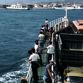 Ferry passengers view coastal fortress and port.