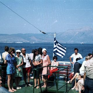 Group of people on ship deck near Greek flag.