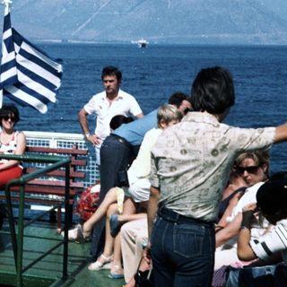 Group of people on ship deck near Greek flag.