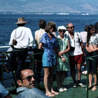 Group of people on ship deck near Greek flag.