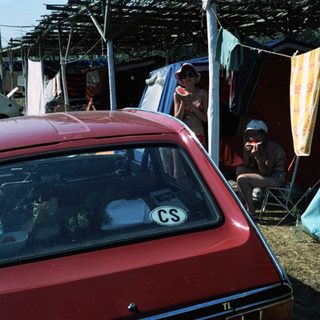 Campsite with tents, car, and people relaxing outdoors.