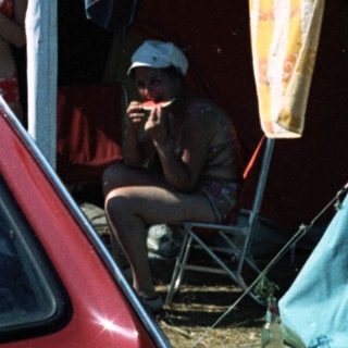 Campsite with tents, car, and people relaxing outdoors.
