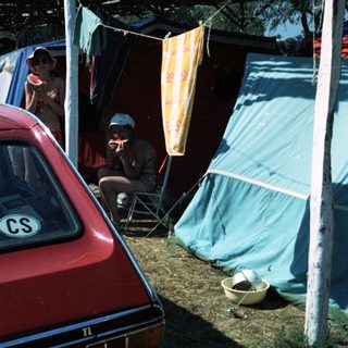 Campsite with tents, car, and people relaxing outdoors.
