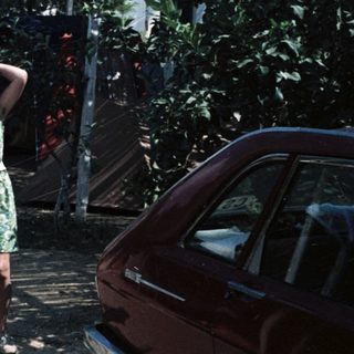 Vintage cars parked in dusty area with woman in green dress.