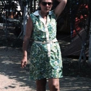 Vintage cars parked in dusty area with woman in green dress.