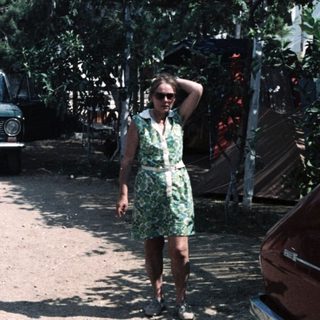 Vintage cars parked in dusty area with woman in green dress.