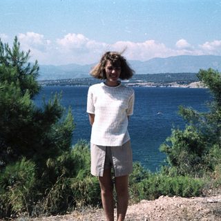 Woman standing by coastal view with sea and mountains.