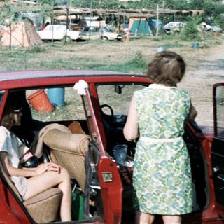 Rural campsite with cars and tents in mountainous area.