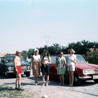 Group posing by vintage cars in rural setting.