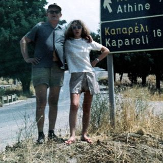 Couple standing by Greek road sign to Athens and Kapareli.