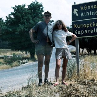 Couple standing by Greek road sign to Athens and Kapareli.
