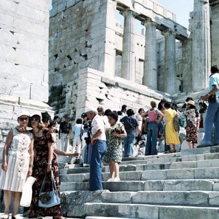 Ancient Greek ruins with tourists ascending steps.