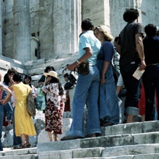 Ancient Greek ruins with tourists ascending steps.