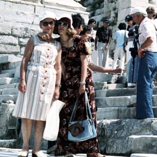 Ancient Greek ruins with tourists ascending steps.