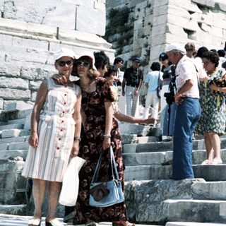 Ancient Greek ruins with tourists ascending steps.