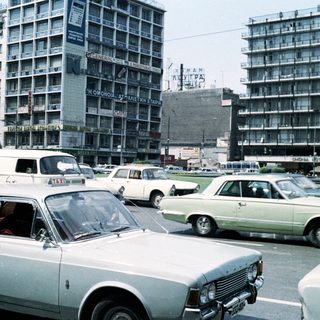 Vintage urban traffic with mid-century cars and high-rise buildings.