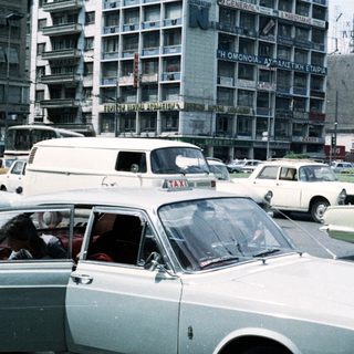 Vintage urban traffic with mid-century cars and high-rise buildings.