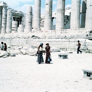 Ancient ruins with partially standing columns, people walking.
