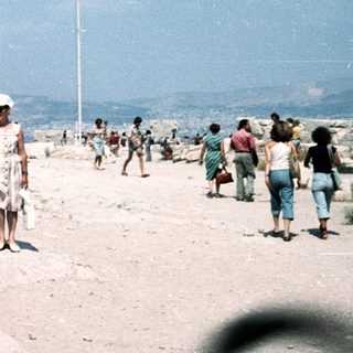 People walking on rocky coastal terrain near unfinished building.