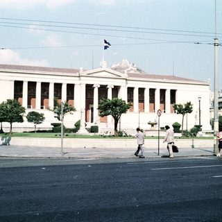 Neoclassical building with Greek flag, urban street scene.