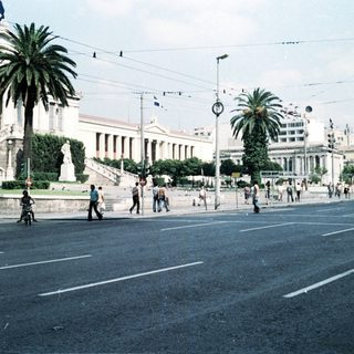 Neoclassical building in urban square with pedestrians.