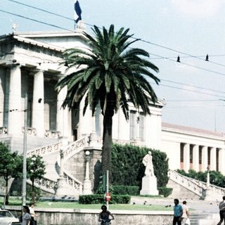 Neoclassical building in urban square with pedestrians.