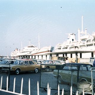 Port with vintage cars parked near large cruise ships.