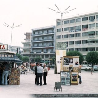Busy urban square with street vendors and mid-20th-century buildings.
