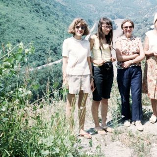 Five people posing outdoors by a vehicle on a scenic hillside.