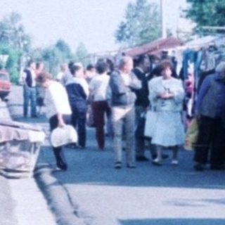Outdoor flea market with stalls and parked cars.