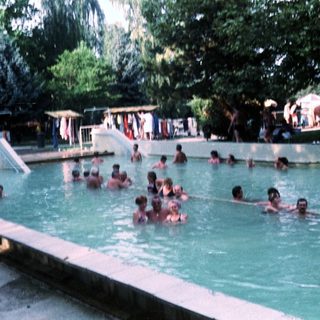 Outdoor swimming pool with many people enjoying water.