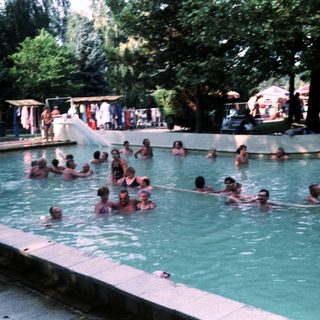 Outdoor swimming pool with many people enjoying water.