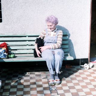 Woman with purple hair sits on bench holding black dog.