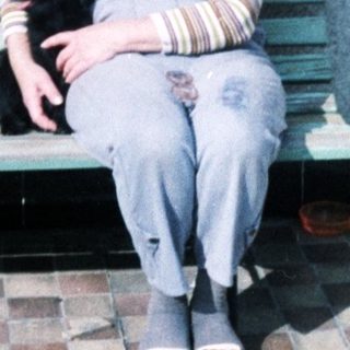 Woman with purple hair sits on bench holding black dog.