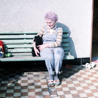 Woman with purple hair sits on bench holding black dog.