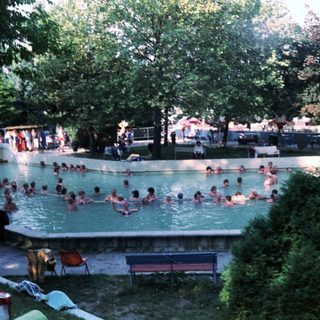 Outdoor swimming pool with many people relaxing.