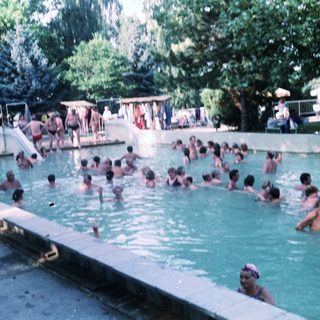 Busy outdoor swimming pool with many people enjoying water.